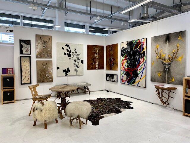 Messestand von Evdokia Kulikova auf der ARTMUC München 2024: mehrere Fellmalerei-Werke an weißen Wänden, dazu Hocker aus Schaffell und Beistelltische aus Geweih