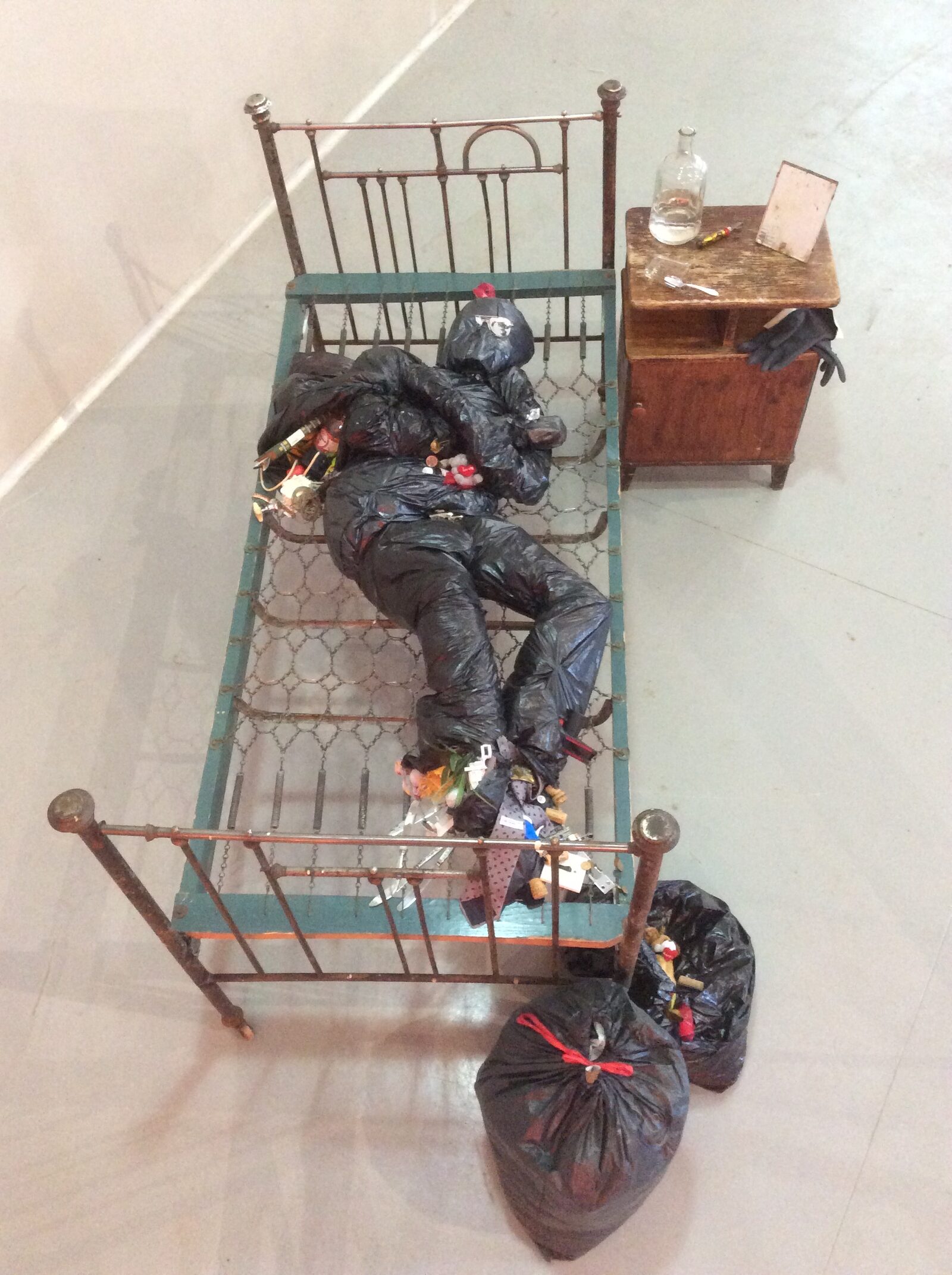 Metallbett mit Müllsack-Figur, Seitenansicht
