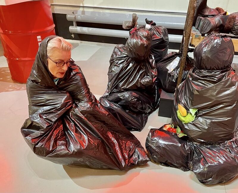 Zwei kauernde Figuren aus schwarzen Müllsäcken, dahinter die Künstlerin