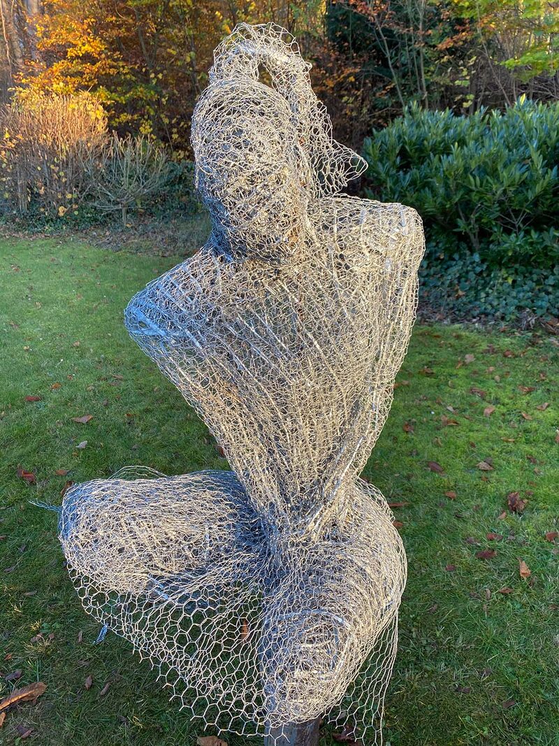 Lebensgroße sitzende Frauenfigur aus Drahtgeflecht im Garten, Nahansicht